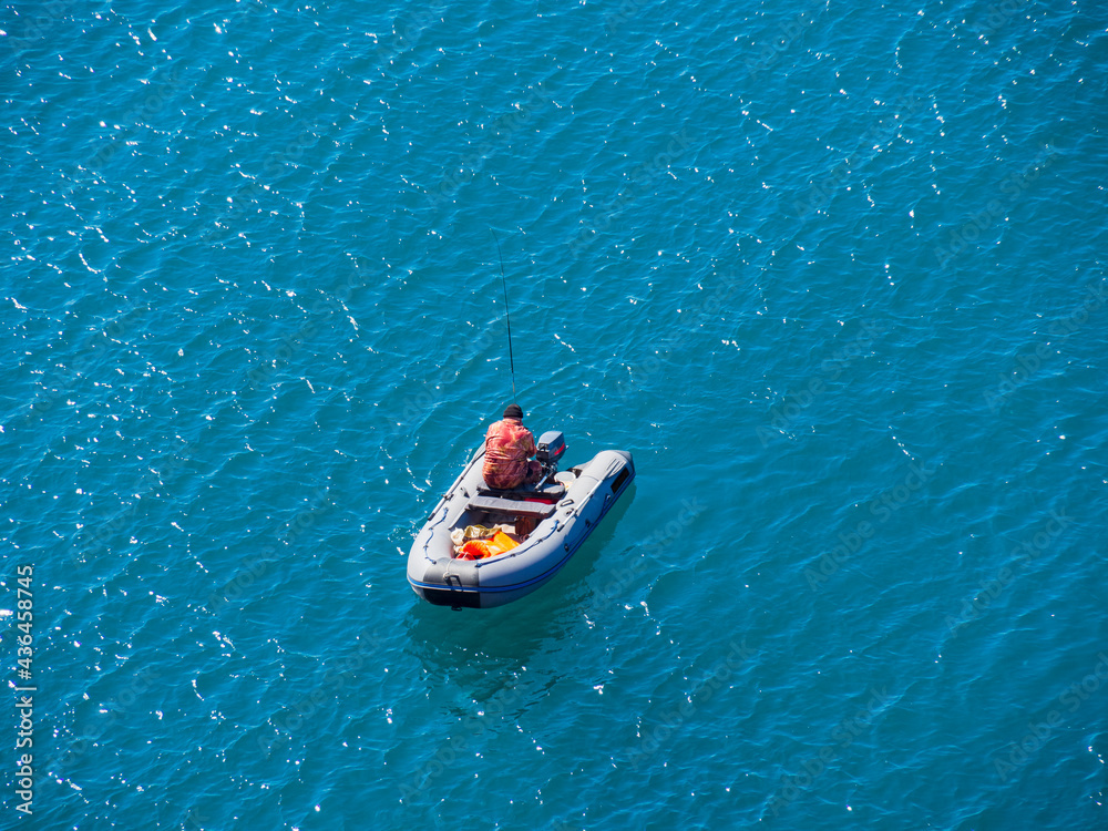 A lone boat with industrial fishermen in the open sea with a rod and nets. The concept of poaching and illegal fishing.