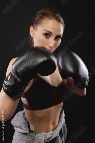 Portrait Caucasian fitness girl in boxing gloves stands in a rack on a black background, portrait of a strong and independent woman fighter