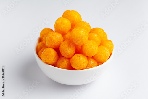 Close up of Cheese Potato Puff Ball Snacks, tangy orange color, Popular Ready to eat crunchy and puffed snacks,  salty in white ceramic bowl over white background