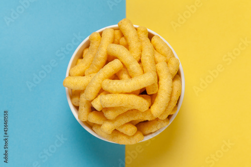 Close up of Cheese Potato Puff Snacks sticks, Popular Ready to eat crunchy and puffed snacks sticks cheesy salty pale-yellow color over Blue-Yellow background