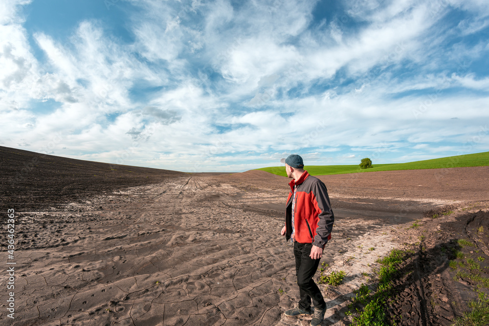 A male agronomist examines the fields after heavy rains against the backdrop of rainy clouds. Weather damage assessment agricultural land after flood