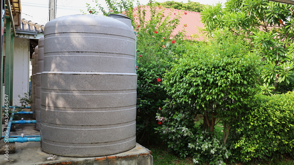 Cream colored water tank on concrete base. Multiple plastic water tanks