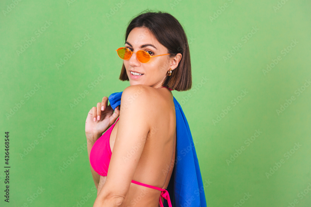 Summer fit sporty woman in pink bikini, blue shirt and orange sunglasses on green background, happy cheerful joyful positive