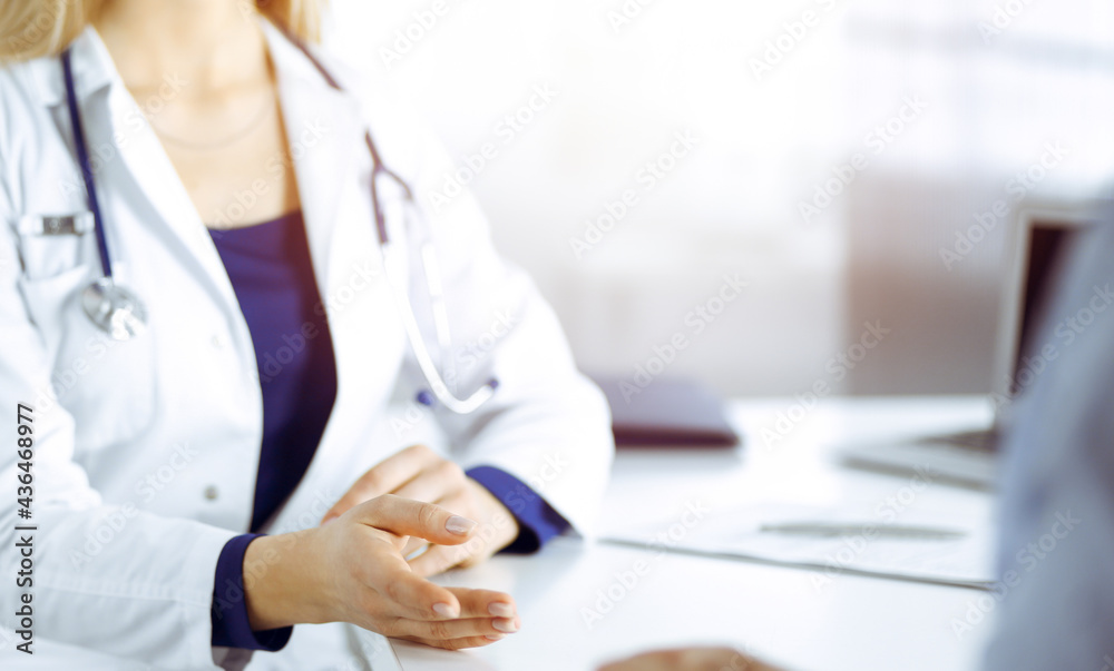 Unknown woman-doctor is talking to her patient, while they are sitting together in the sunny cabinet in a clinic. Female physician with a stethoscope at work, close-up. Perfect medical service in a Unknown woman-doctor is talking to her patient, while they are sitting together in the sunny cabinet in a clinic. Female physician with a stethoscope at work, close-up. Perfect medical service in a