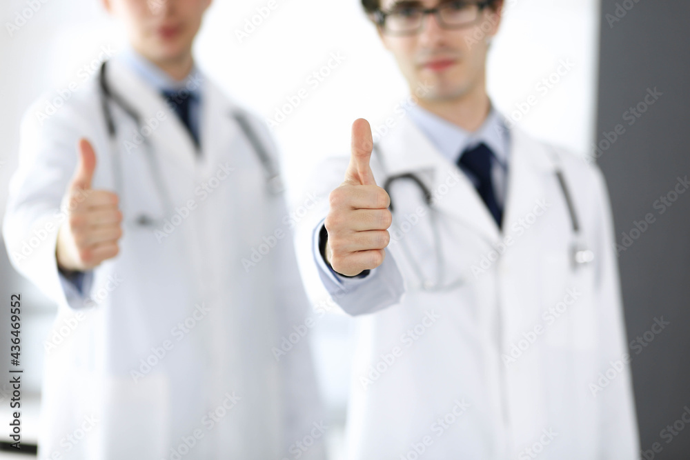 Two male doctors standing as a team and showing thumbs up as a symbol of the best service for patients in the clinic. Medicine and health care Two male doctors standing as a team and showing thumbs up as a symbol of the best service for patients in the clinic. Medicine and health care