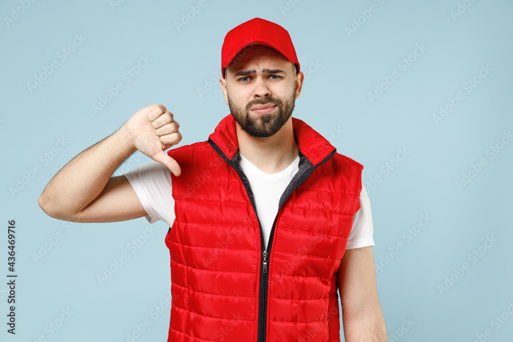 Professional sad tired worry delivery guy employee man in red cap white T-shirt vest uniform workwear work as dealer courier isolated on pastel blue color background studio portrait. Service concept. Professional sad tired worry delivery guy employee man in red cap white T-shirt vest uniform workwear work as dealer courier isolated on pastel blue color background studio portrait. Service concept.