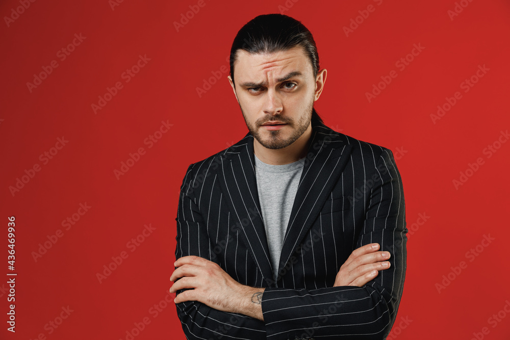 Fototapeta premium Young serious shrewd confident strict businessman latin man in black striped jacket grey shirt hold hands crossed folded isolated on red background studio studio portrait. Concept of people lifestyle.