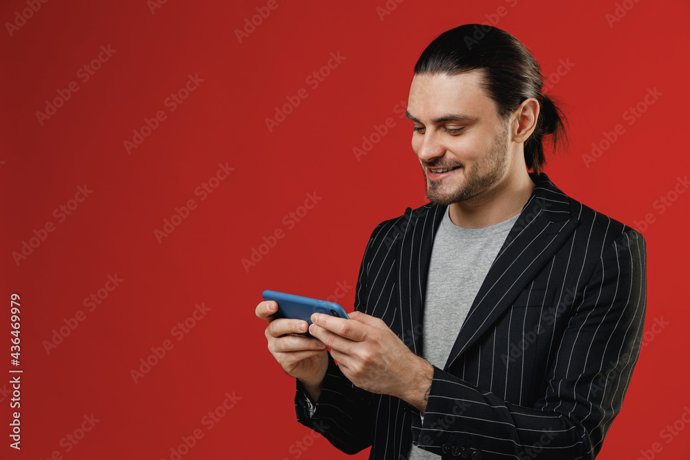 Young fun gambling smiling joyful businessman latin man in black striped jacket grey shirt using play racing on mobile cell phone hold gadget smartphone for pc video games isolated on red background Young fun gambling smiling joyful businessman latin man in black striped jacket grey shirt using play racing on mobile cell phone hold gadget smartphone for pc video games isolated on red background