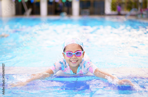 Asian child cute or kid girl wearing swimming suit and goggles on edge swimming pool and smile with happy fun in water park for learn and enjoy training swim or refreshing to exercise on summer school