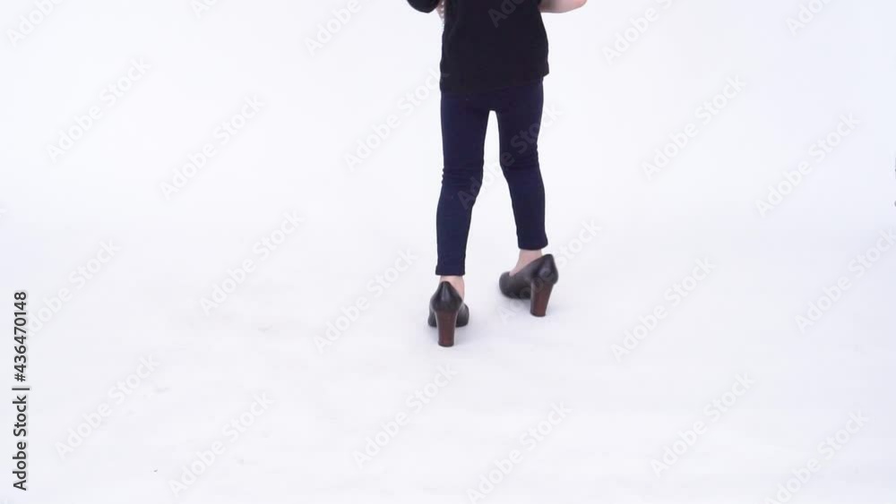 A little girl in oversized shoes on a white background space for text, closeup on legs. Studio shooting without a face A little girl in oversized shoes on a white background space for text, closeup on legs. Studio shooting without a face