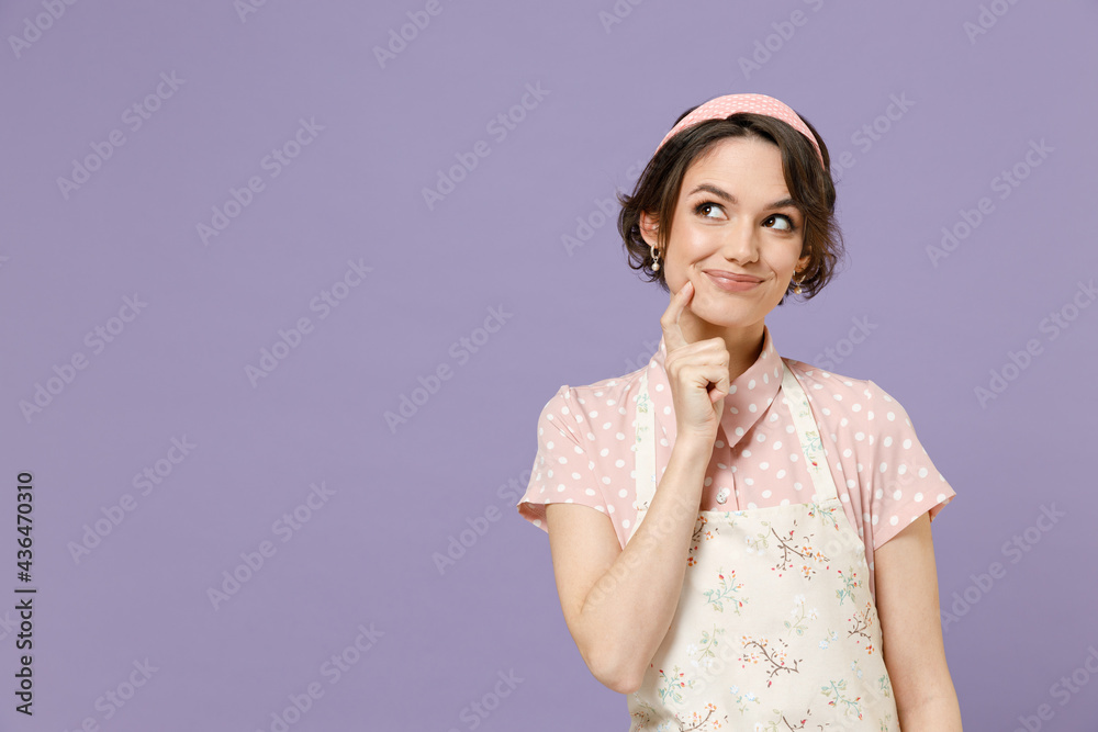 Young thoughtful pensive housewife housekeeper chef cook baker woman wear pink apron t-shirt look aside prop up chin isolated on pastel violet color background studio portrait. Cooking food concept