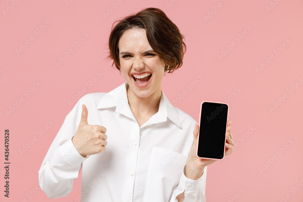 Young employee business woman corporate lawyer in classic formal white shirt work in office hold mobile cell phone blank screen area workspace show thumb up gesture isolated on pastel pink background Young employee business woman corporate lawyer in classic formal white shirt work in office hold mobile cell phone blank screen area workspace show thumb up gesture isolated on pastel pink background