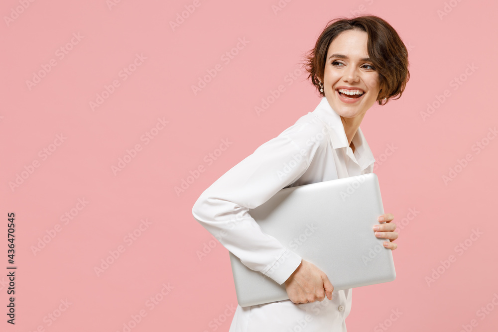 Side view young employee business secretary woman corporate lawyer in classic formal white shirt work in office hold closed laptop pc computer chat online isolated on pastel pink background studio Side view young employee business secretary woman corporate lawyer in classic formal white shirt work in office hold closed laptop pc computer chat online isolated on pastel pink background studio