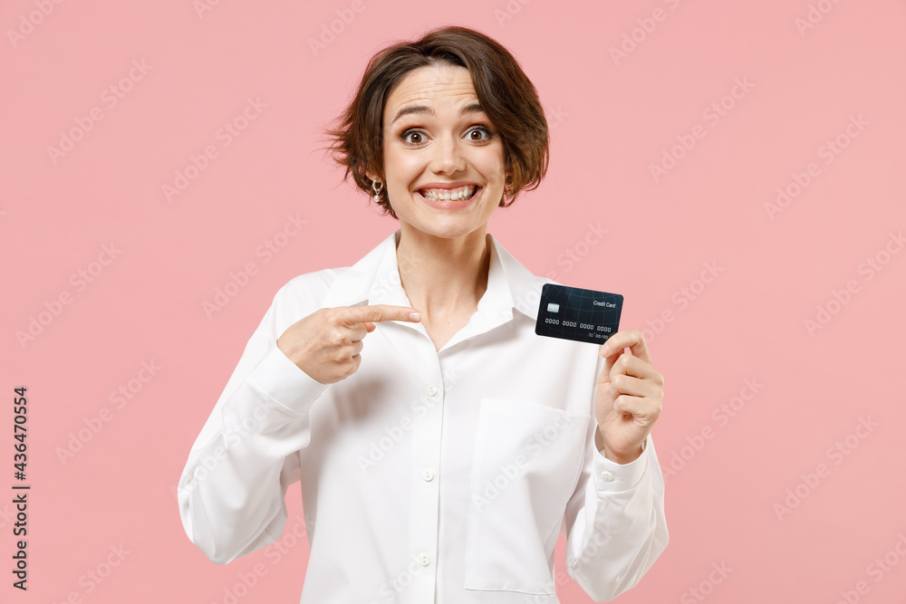 Fun young employee business secretary woman 20s corporate lawyer in classic formal white shirt work in office point index finger on credit bank card isolated on pastel pink background studio portrait. Fun young employee business secretary woman 20s corporate lawyer in classic formal white shirt work in office point index finger on credit bank card isolated on pastel pink background studio portrait.
