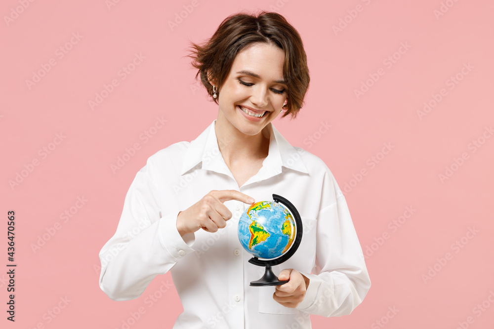 Fototapeta premium Happy fun smiling young employee business secretary woman 20s corporate lawyer wear classic formal white shirt work in office spin touch Earth world globe isolated on pastel pink background studio