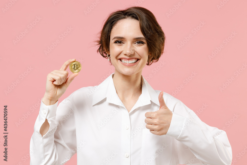 Young successful employee business secretary woman corporate lawyer in classic formal white shirt work in office holding bitcoin coin currency show thumb up gesture isolated on pastel pink background Young successful employee business secretary woman corporate lawyer in classic formal white shirt work in office holding bitcoin coin currency show thumb up gesture isolated on pastel pink background