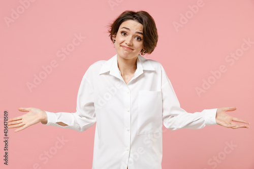 Young doubtful employee business woman corporate lawyer in classic formal white shirt work in office shrugging shoulders look puzzled have no idea nothing to say isolated on pastel pink background
