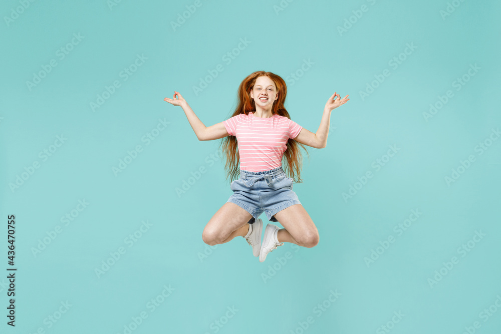 Full length little redhead kid girl 12-13 year old wear pink t-shirt hold hands in yoga om gesture relax meditate calm down isolated on pastel blue background Children lifestyle childhood concept.