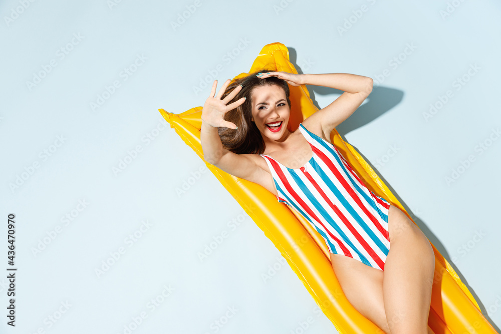 Top view beautiful young sexy woman slim body wear striped one-piece swimsuit lies on inflatable mattress hotel pool isolated on pastel blue color background. Summer vacation sea rest sun tan concept.