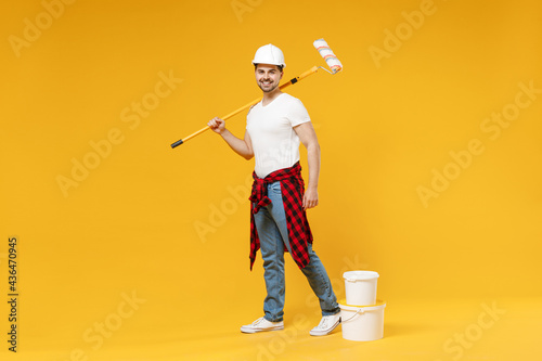 Full length fun young employee handyman man wear t-shirt holding paint roller look camera walk isolated on yellow background Instruments accessories for renovation apartment room. Repair home concept.