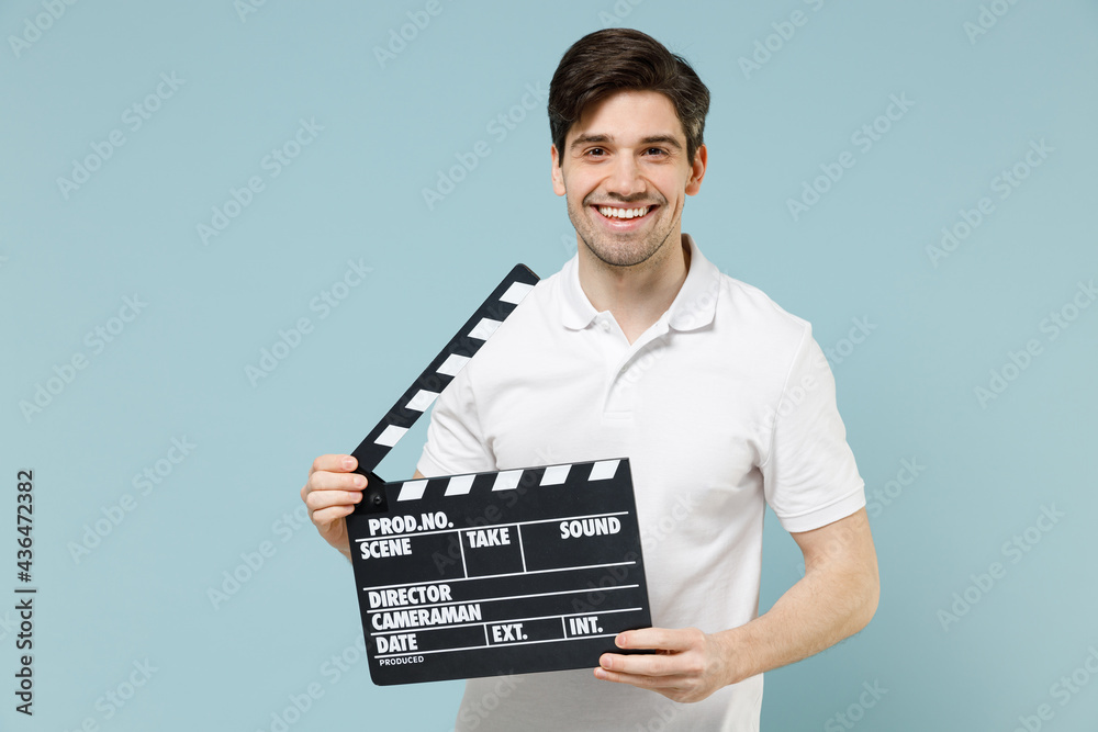 Naklejka premium Young happy cheerful man 20s wear white casual basic t-shirt polo holding in hands classic black film making clapperboard isolated on pastel blue background studio portrait People lifestyle concept