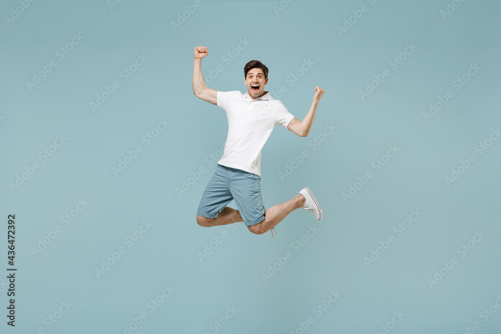 Full length young fun happy caucasian man 20s wear white casual basic t-shirt do winner gesture clench fist jump high isolated on pastel blue color background studio portrait People lifestyle concept