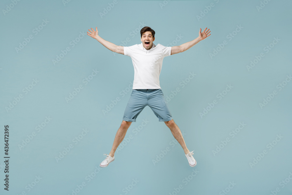 Full length young fun happy caucasian man 20s wearing white casual basic t-shirt jump high with outstretched hands isolated on pastel blue color background studio portrait. People lifestyle concept.