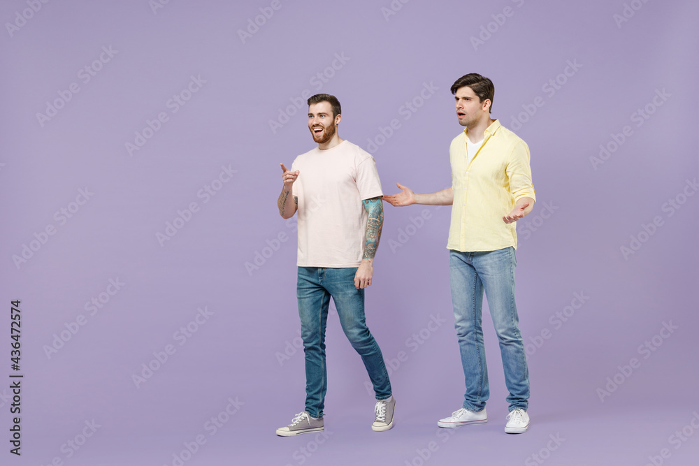 Full length shocked amazed two young men friends together in casual t-shirt walk go point finger aside spread hands isolated on purple background studio portrait People friendship lifestyle concept Full length shocked amazed two young men friends together in casual t-shirt walk go point finger aside spread hands isolated on purple background studio portrait People friendship lifestyle concept