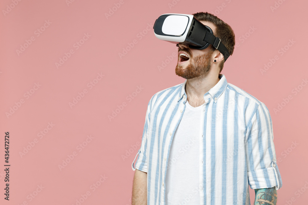 Young excited happy fun surprised amazed happy caucasian unshaven man 20s wearing blue striped shirt playing watching in vr headset pc gadget isolated on pastel pink color background studio portrait Young excited happy fun surprised amazed happy caucasian unshaven man 20s wearing blue striped shirt playing watching in vr headset pc gadget isolated on pastel pink color background studio portrait