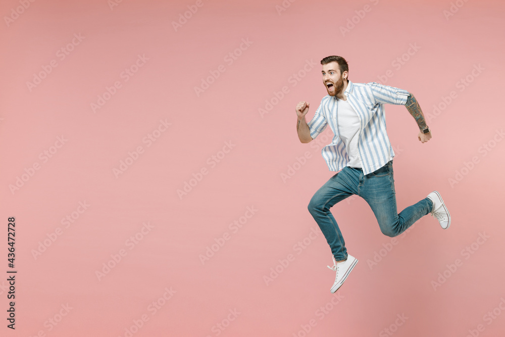 Full length side view sporty young caucasian unshaven man 20s wearing blue striped shirt white t-shirt jump high run fast hurry up isolated on pastel pink color background. People lifestyle concept.