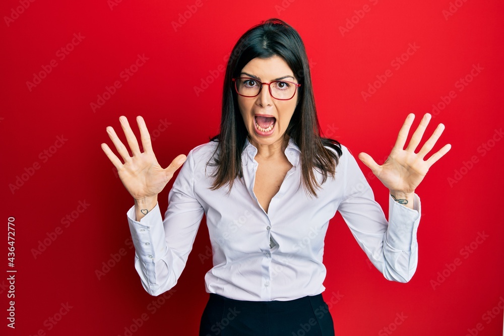 Young hispanic woman wearing business shirt and glasses celebrating crazy and amazed for success with arms raised and open eyes screaming excited. winner concept Young hispanic woman wearing business shirt and glasses celebrating crazy and amazed for success with arms raised and open eyes screaming excited. winner concept