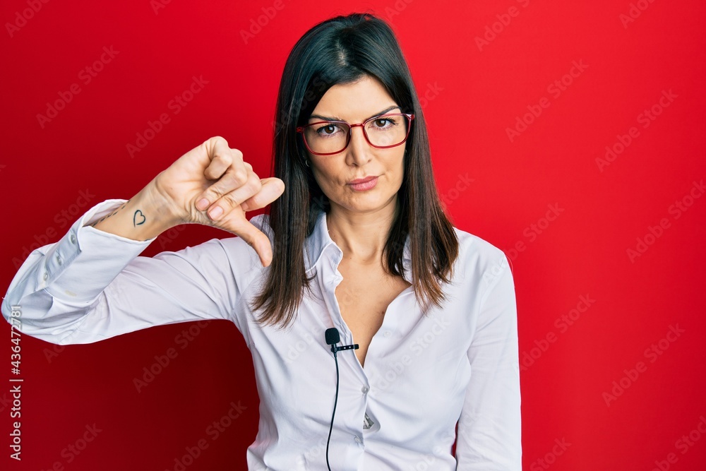 Young hispanic woman using lavalier microphone with angry face, negative sign showing dislike with thumbs down, rejection concept Young hispanic woman using lavalier microphone with angry face, negative sign showing dislike with thumbs down, rejection concept