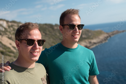 Twin brothers posing infront of the ocean wearing sunglasses in a summer day.