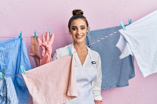 Beautiful brunette young woman washing clothes at clothesline showing and pointing up with fingers number four while smiling confident and happy.