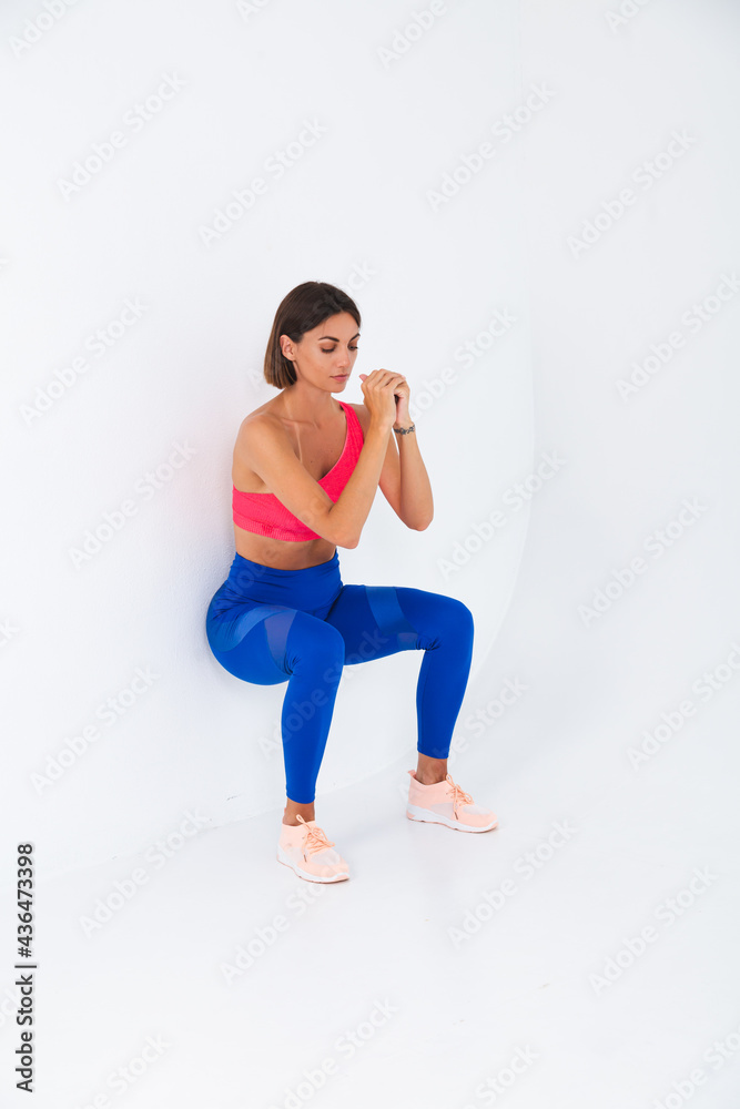 Fit tanned sporty woman with abs, fitness curves, wearing top and blue leggings on white background does chair exercise
