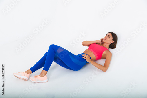 Fit tanned sporty woman with abs, fitness curves, wearing top and blue leggings on white background