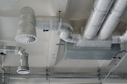 Ventilation pipes in silver insulation material hanging from the ceiling inside new building. System of industrial ventilating pipes. Air flow and ventilation system.