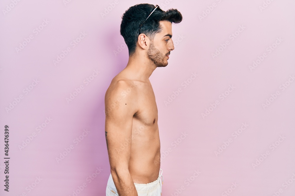 Fototapeta premium Young hispanic man wearing swimwear shirtless looking to side, relax profile pose with natural face with confident smile.