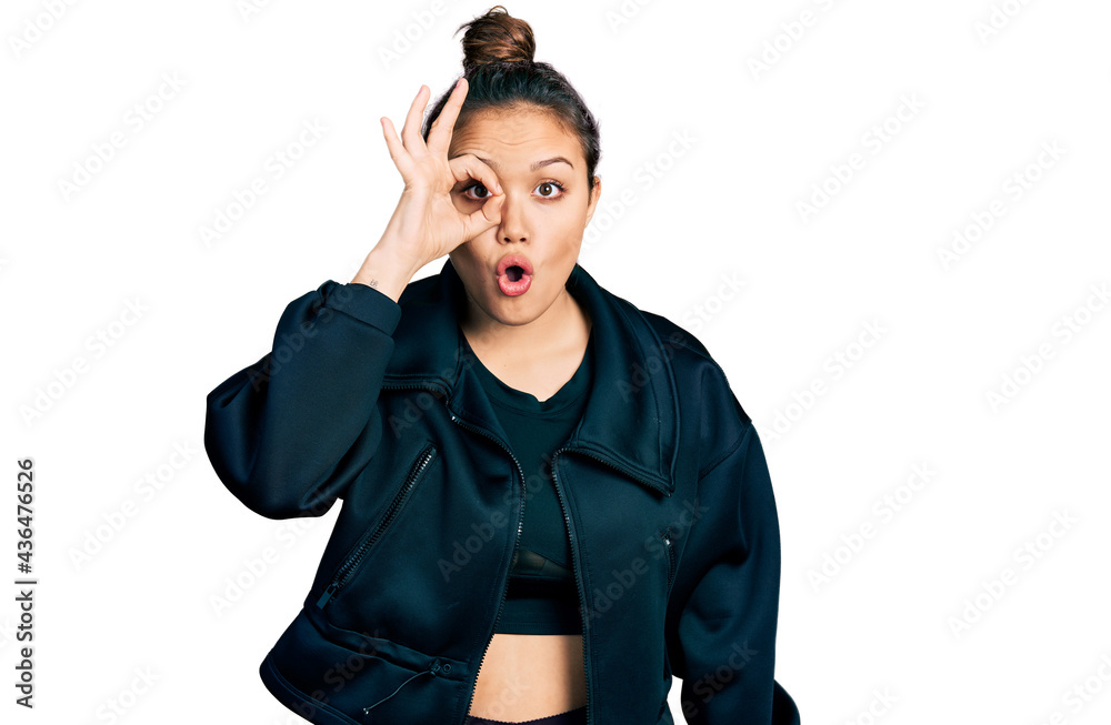 Young hispanic girl wearing sportswear doing ok gesture shocked with surprised face, eye looking through fingers. unbelieving expression. Young hispanic girl wearing sportswear doing ok gesture shocked with surprised face, eye looking through fingers. unbelieving expression.