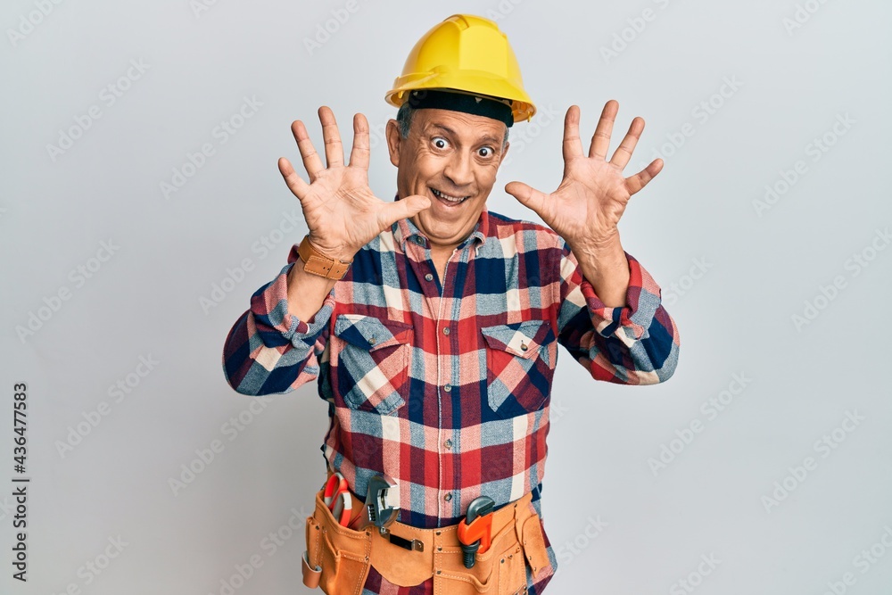 Senior hispanic man wearing handyman uniform showing and pointing up with fingers number ten while smiling confident and happy. Senior hispanic man wearing handyman uniform showing and pointing up with fingers number ten while smiling confident and happy.
