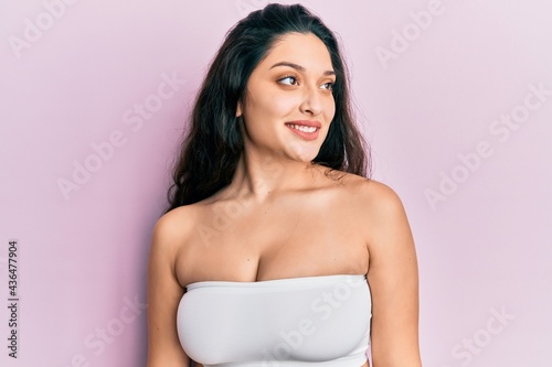 Beautiful middle eastern woman standing wearing a top showing skin looking to side, relax profile pose with natural face and confident smile.