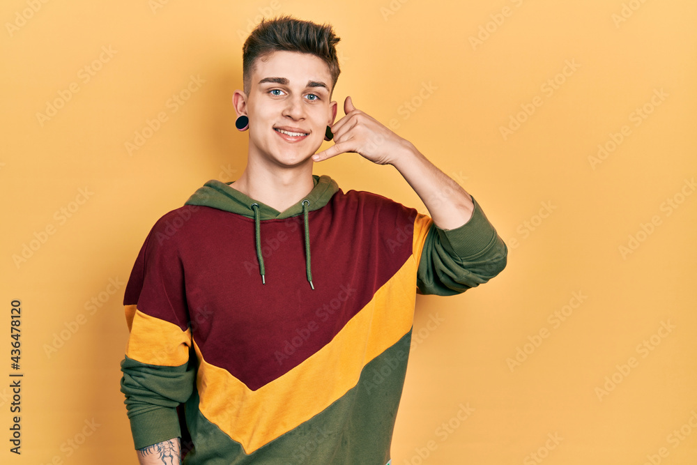 Young caucasian boy with ears dilation wearing casual sweatshirt smiling doing phone gesture with hand and fingers like talking on the telephone. communicating concepts. Young caucasian boy with ears dilation wearing casual sweatshirt smiling doing phone gesture with hand and fingers like talking on the telephone. communicating concepts.