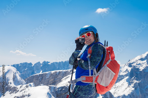 beautiful sporty girl climber takes photos on a small camera from the top of the conquered peak 