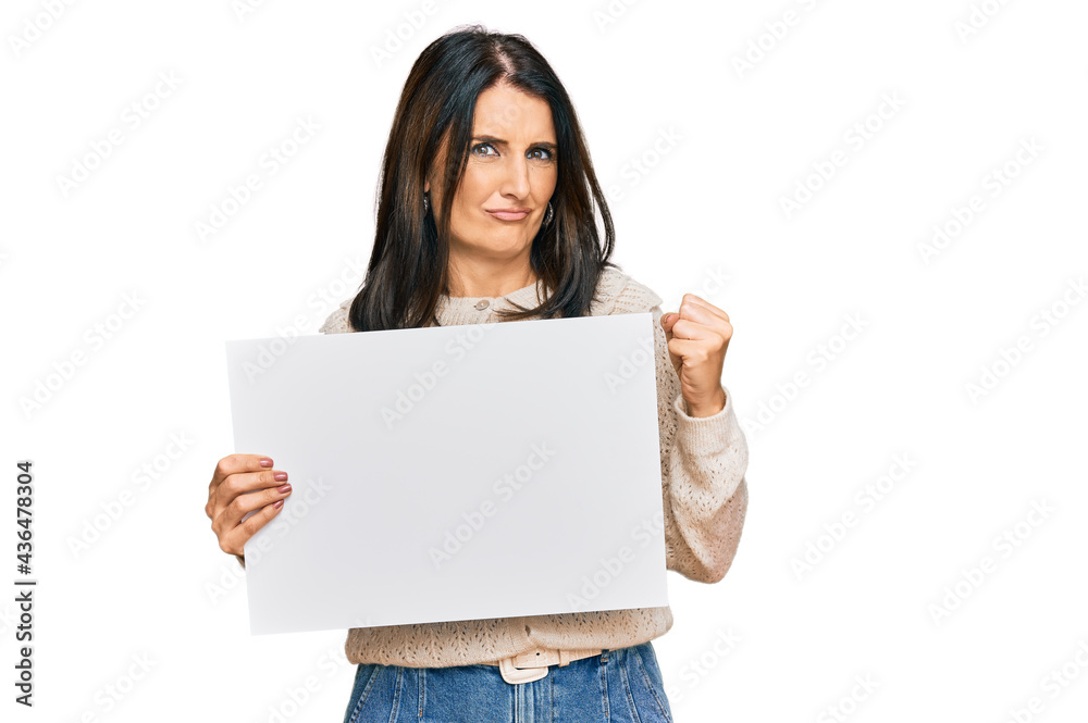 Middle age brunette woman holding blank empty banner screaming proud, celebrating victory and success very excited with raised arms Middle age brunette woman holding blank empty banner screaming proud, celebrating victory and success very excited with raised arms