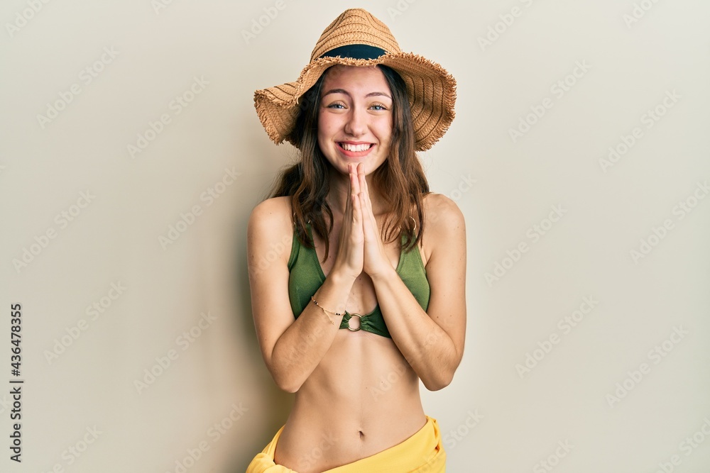 Young brunette woman wearing bikini praying with hands together asking for forgiveness smiling confident. Young brunette woman wearing bikini praying with hands together asking for forgiveness smiling confident.