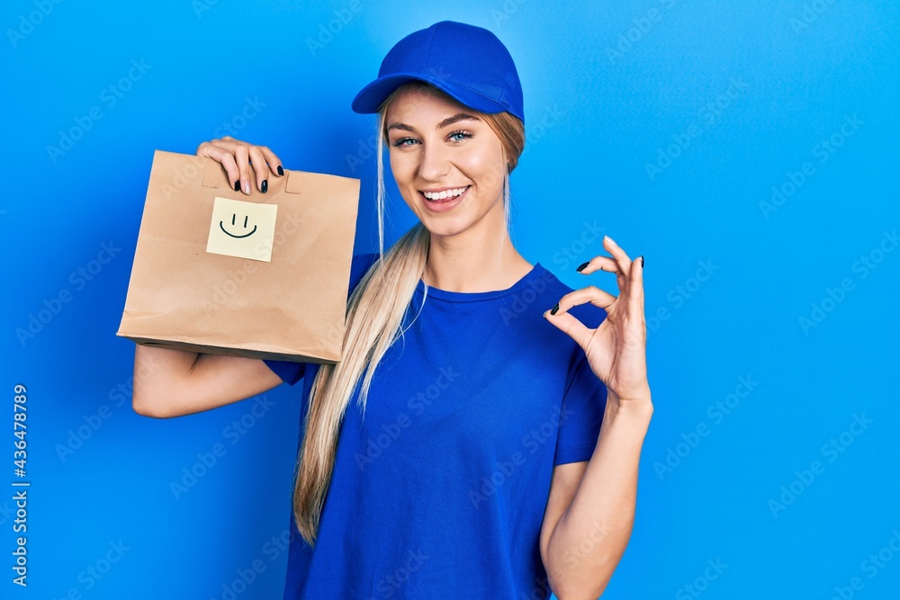 Young caucasian woman holding take away paper bag with happy face reminder doing ok sign with fingers, smiling friendly gesturing excellent symbol Young caucasian woman holding take away paper bag with happy face reminder doing ok sign with fingers, smiling friendly gesturing excellent symbol