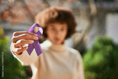 Fotografie Young hispanic girl with serious expression holding purple awareness ribbon at the city