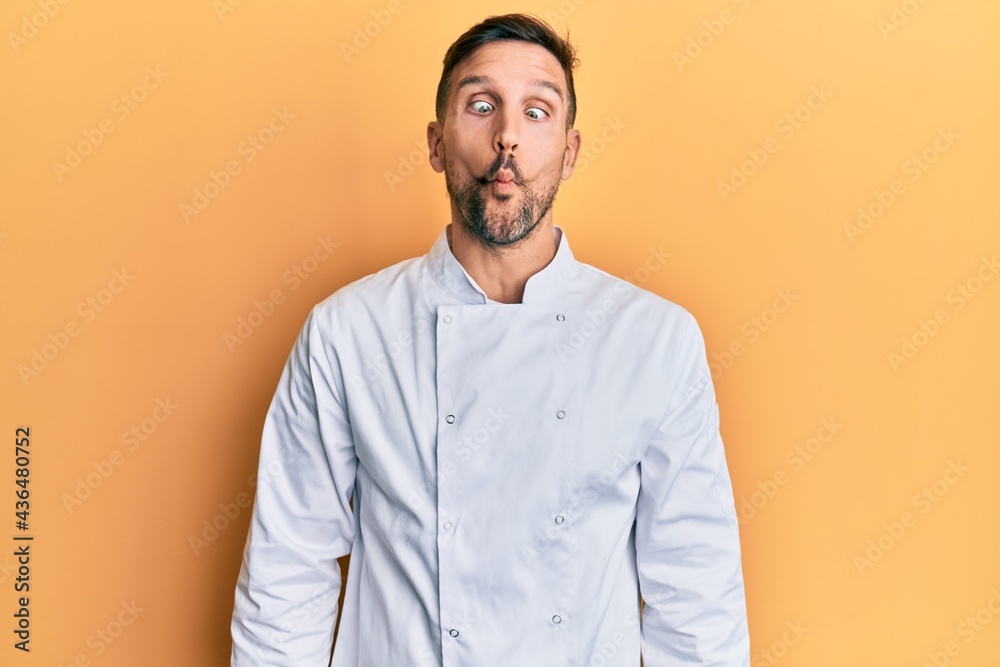 Handsome man with beard wearing professional cook uniform making fish face with lips, crazy and comical gesture. funny expression. Handsome man with beard wearing professional cook uniform making fish face with lips, crazy and comical gesture. funny expression.
