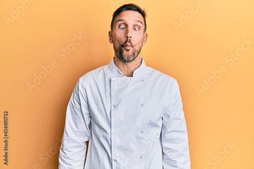 Handsome man with beard wearing professional cook uniform making fish face with lips, crazy and comical gesture. funny expression. © Krakenimages.com