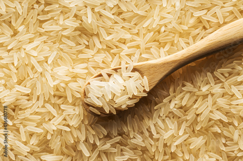 Uncooked, raw long grain rice in a wooden spoon on a background of rice